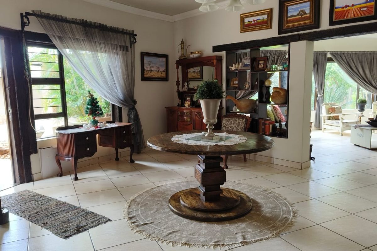 A spacious living area featuring tiled flooring, recessed lighting, and a built-in shelving unit, with an open-plan layout connecting to adjacent living spaces.