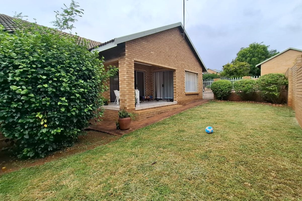 Rear view of a brick house featuring a covered patio area, sliding glass doors, and a private garden with a brick boundary wall.