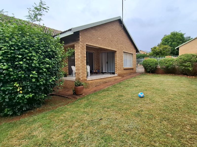 Rear view of a brick house featuring a covered patio area, sliding glass doors, and a private garden with a brick boundary wall.