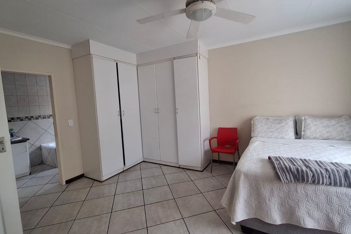 A bedroom featuring built-in cupboards, a ceiling fan, and tiled flooring, with an adjacent view into a tiled bathroom area.