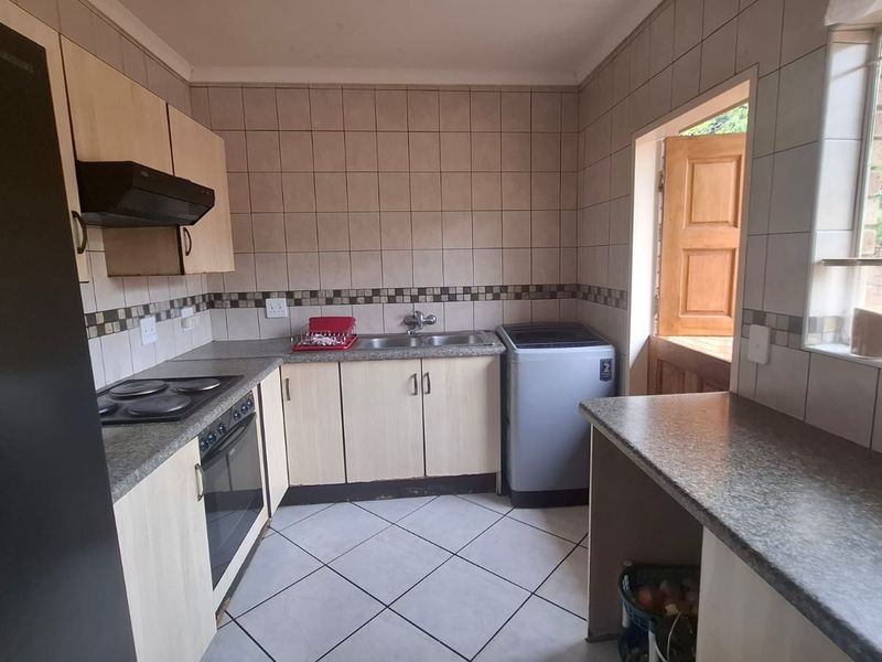 Functional kitchen featuring built-in cabinetry, laminate countertops, electric hob, oven, and tiled finishes with direct access to the exterior.