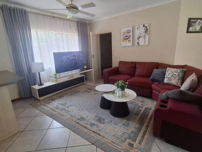 A comfortable living room featuring tiled flooring, a ceiling fan, and large windows with curtain rails, providing a functional and well-lit space.