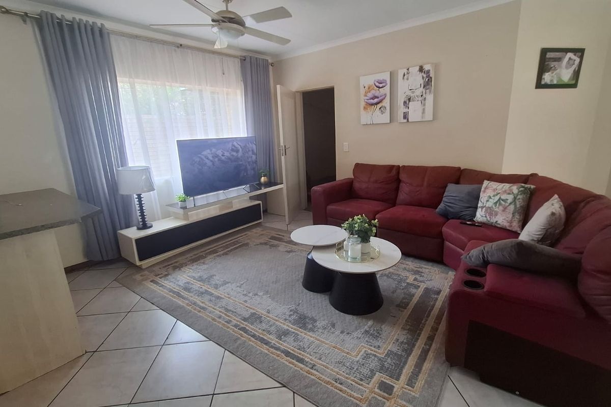 A comfortable living room featuring tiled flooring, a ceiling fan, and large windows with curtain rails, providing a functional and well-lit space.