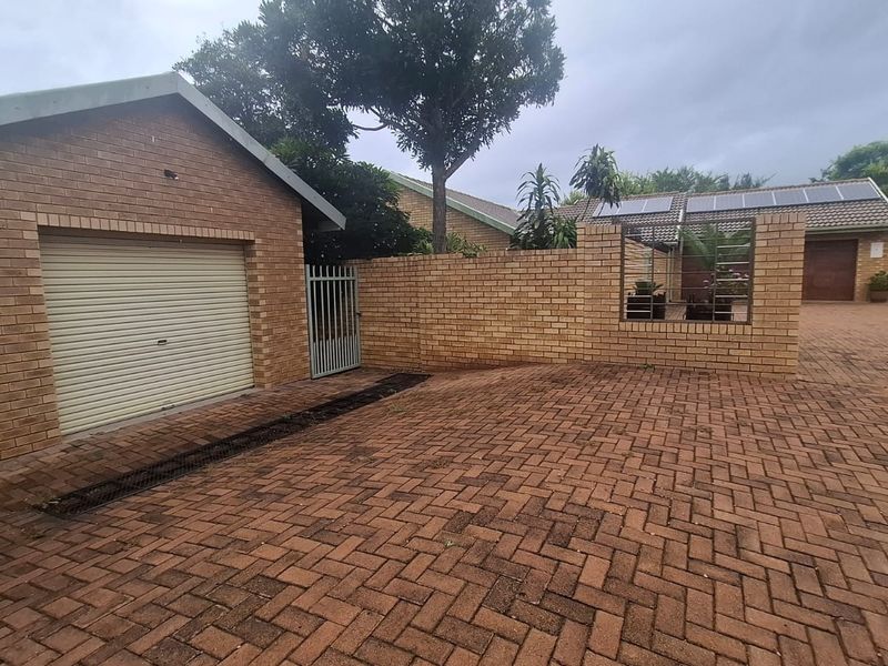 Front exterior view showing a brick-paved driveway, a single garage with a roller door, and a brick boundary wall with a pedestrian gate.