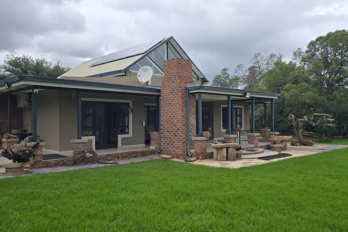 Rear view of a modern house featuring a brick chimney, covered patio area, paved terrace, and solar panels set against a landscaped garden.