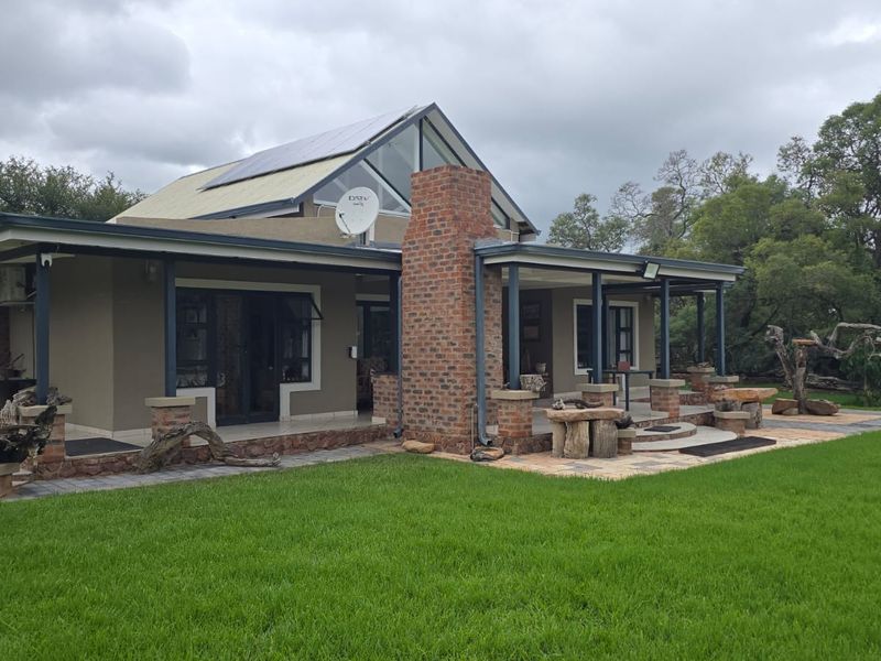 Rear view of a modern house featuring a brick chimney, covered patio area, paved terrace, and solar panels set against a landscaped garden.