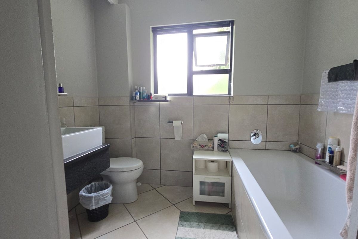 A functional bathroom featuring a bathtub, toilet, and vanity basin with neutral wall and floor tiling.