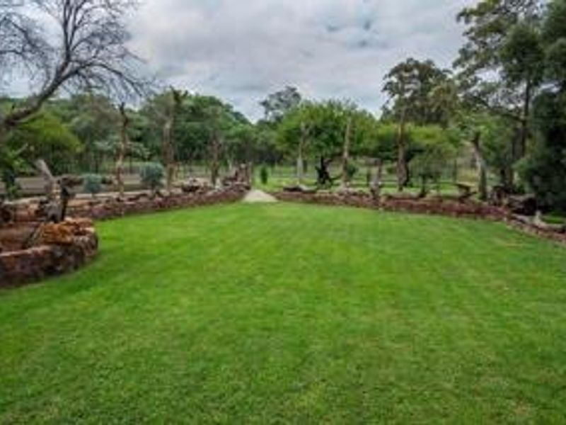 A well-maintained garden featuring a lush green lawn bordered by natural stone retaining walls and mature trees.
