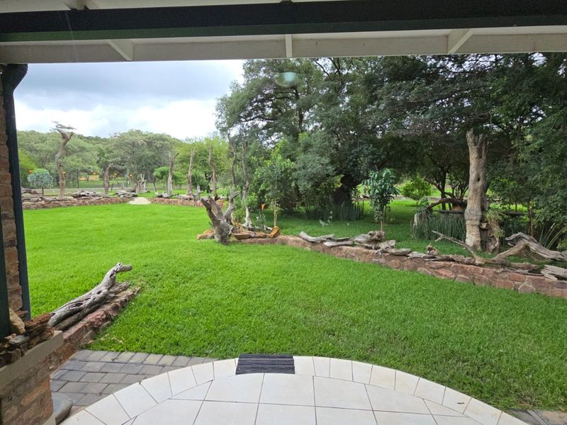 A covered patio area overlooking a spacious, well-maintained garden with stone retaining walls and mature trees.