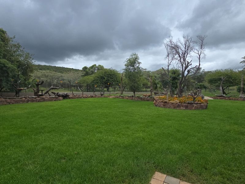 A well-maintained green lawn featuring stone retaining walls and established garden beds, set against a natural landscape backdrop.
