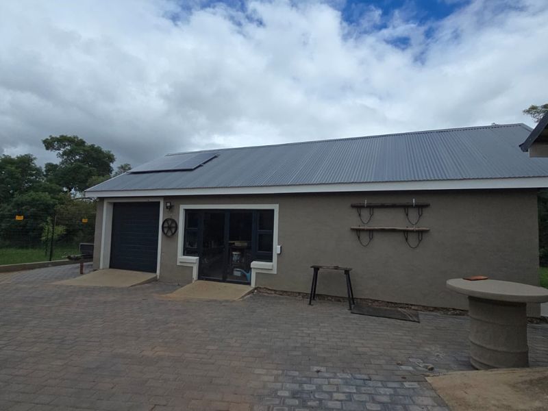 Rear view of the property featuring a paved driveway, garage access, and a corrugated metal roof equipped with solar panels.