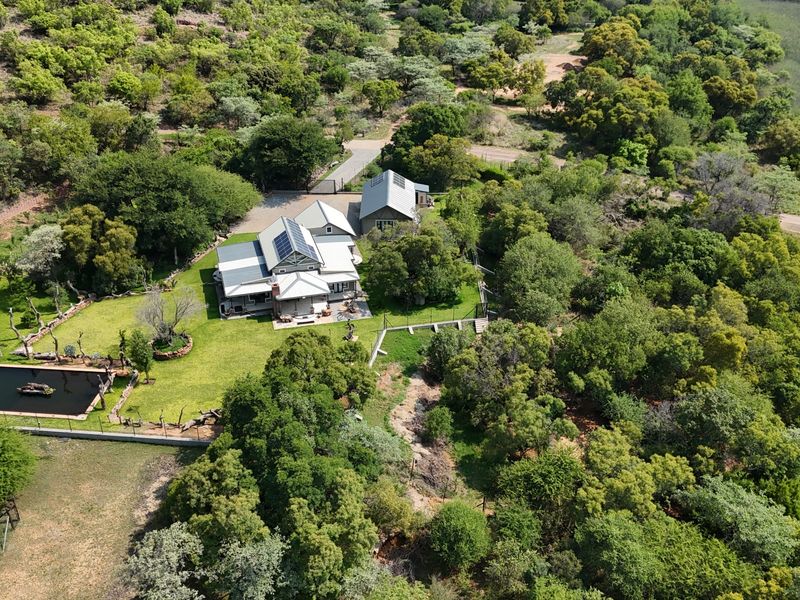 Aerial view of a residential property featuring a main house with solar panels, a swimming pool, and extensive surrounding natural landscape.