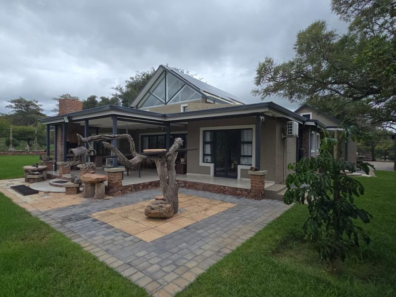 Rear view of the house featuring a paved patio area, brick chimney, and a distinctive pitched roof with a triangular gable window.