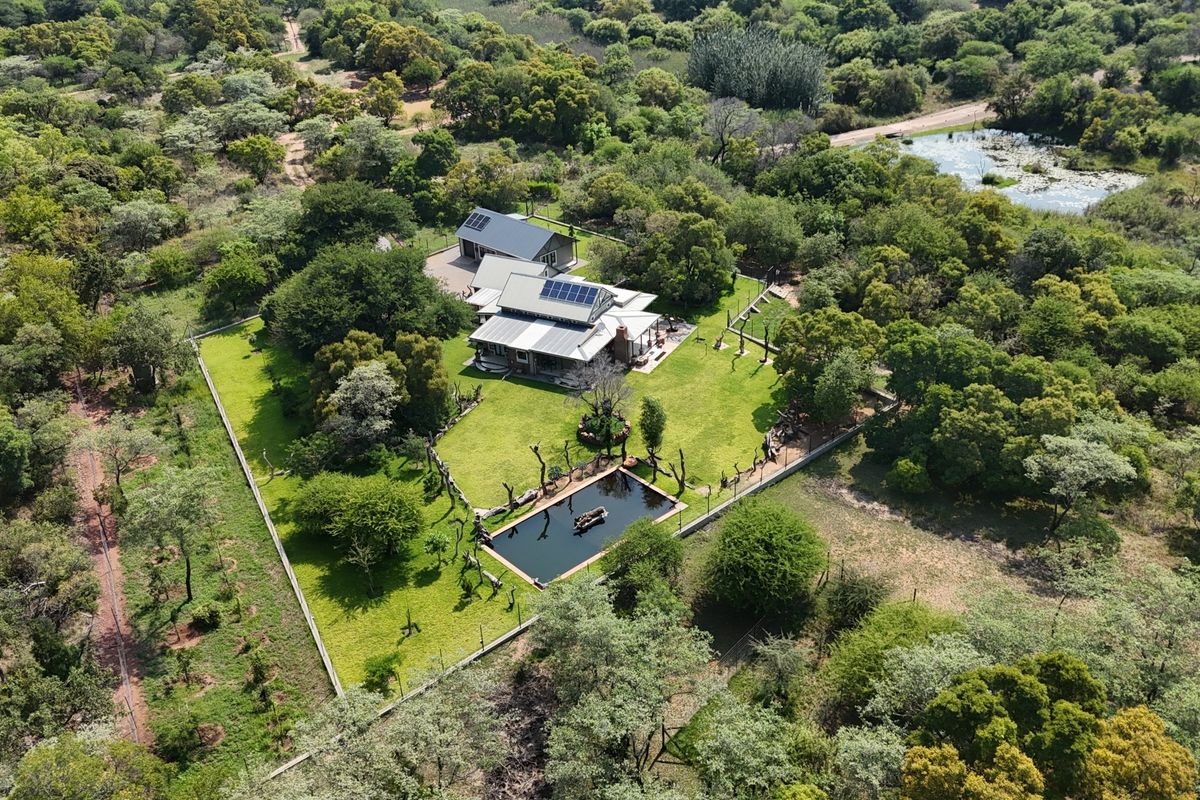 Aerial view of a residential property featuring a main house with solar panels, a swimming pool, and a well-maintained garden in a rural setting.