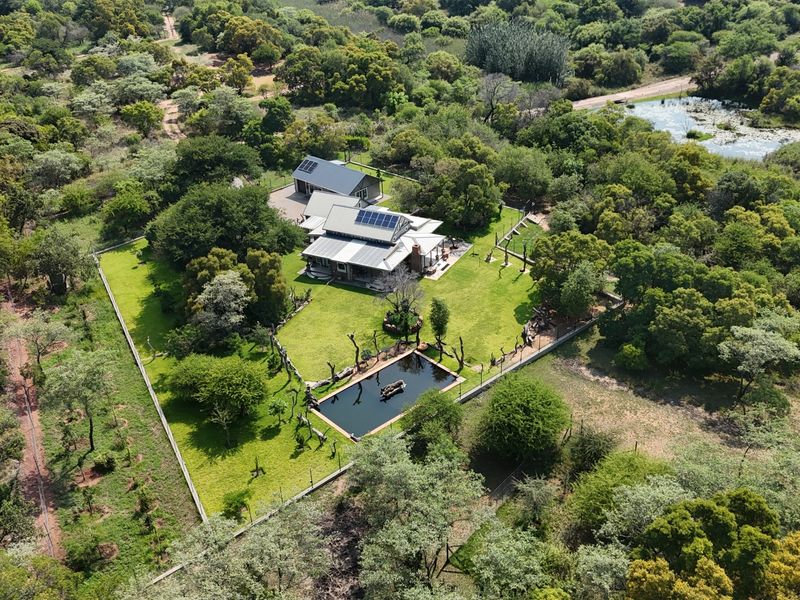 Aerial view of a residential property featuring a main house with solar panels, a swimming pool, and a well-maintained garden in a rural setting.