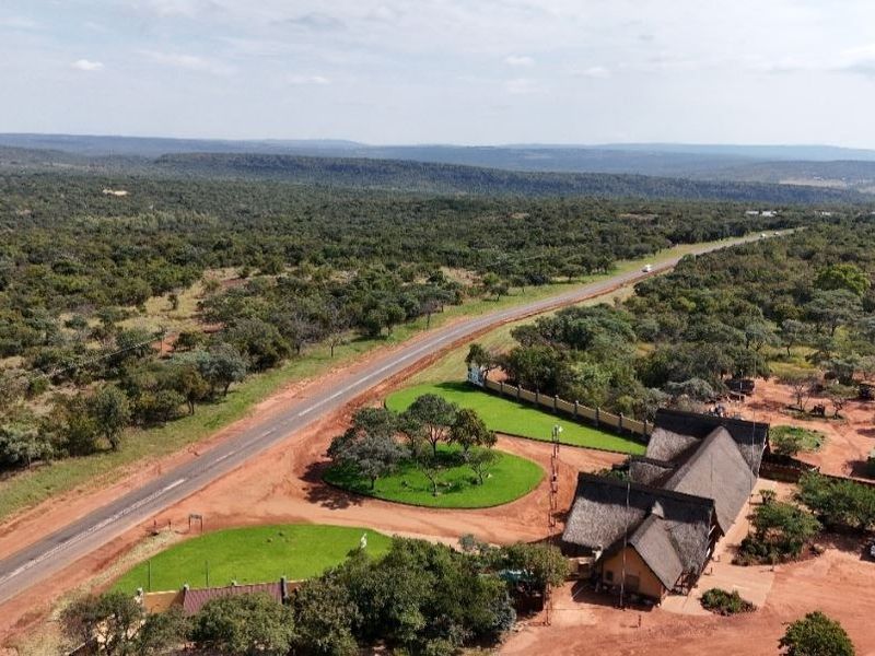 Aerial view of a residential property featuring a thatched-roof building, landscaped grounds, and direct access to a paved road in a rural setting.