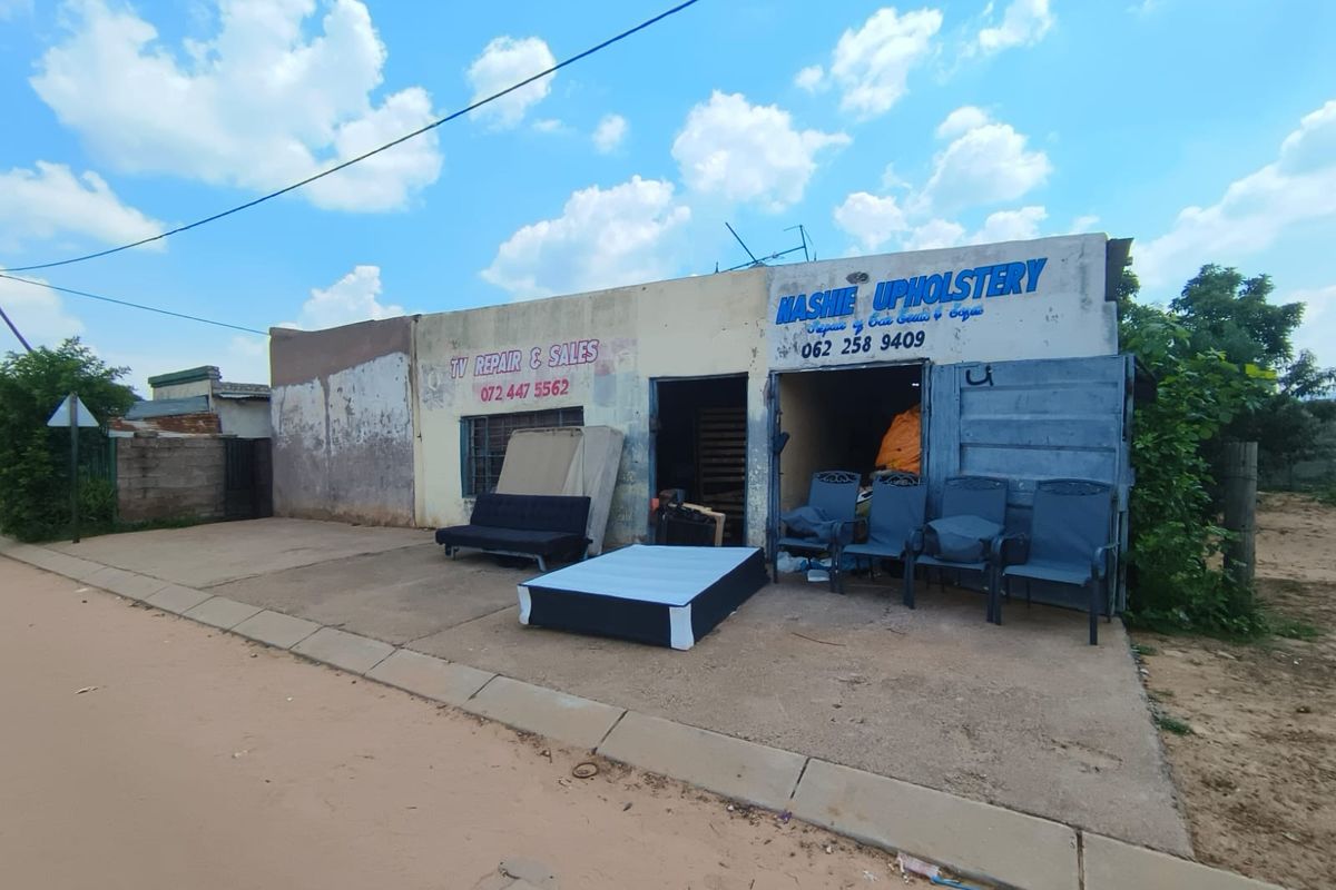 Front exterior view of a commercial property featuring a concrete driveway and signage, showing significant signs of wear and weathering.