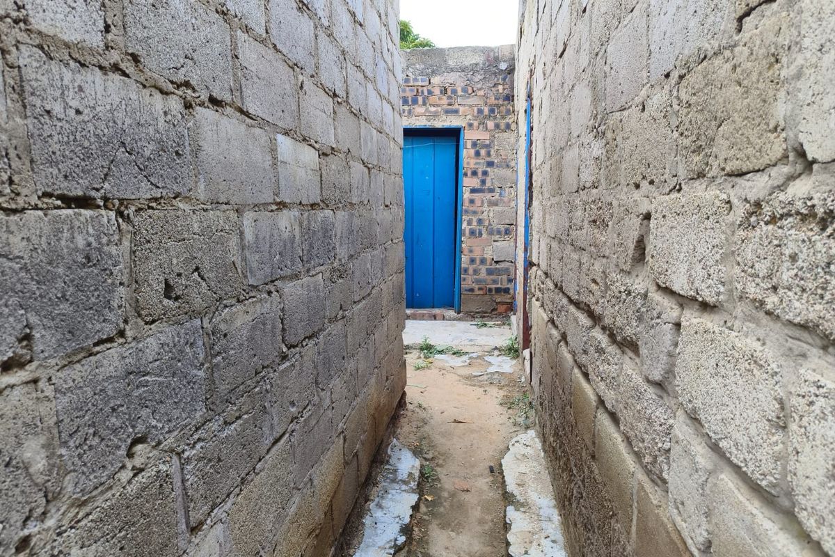 A narrow exterior passage between unfinished concrete block walls leading to a blue door.