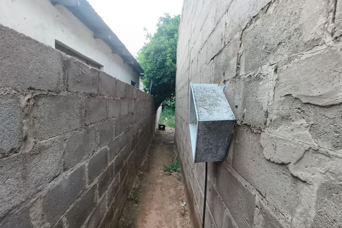 A narrow side passage between two unrendered concrete block walls featuring an external utility box and exposed electrical conduit.