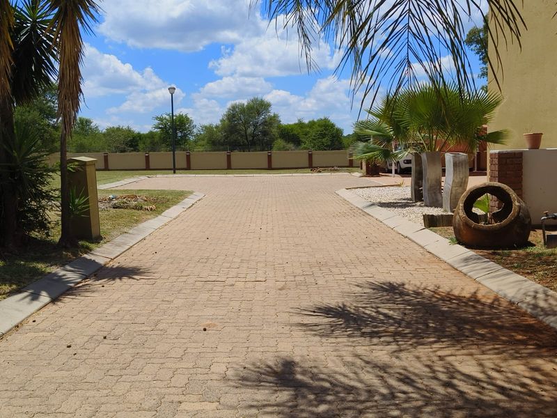 A well-maintained paved driveway leading to the property, featuring a secure perimeter wall and established landscaping.