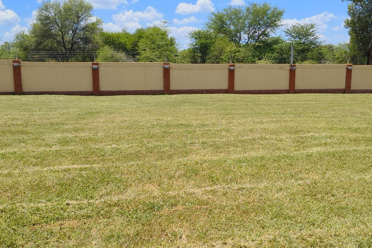 A spacious, level residential plot featuring a well-maintained lawn and a secure perimeter wall with integrated electric fencing and lighting.