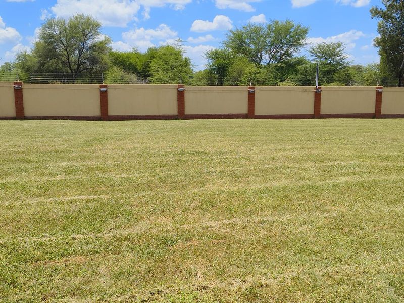 A spacious, level residential plot featuring a well-maintained lawn and a secure perimeter wall with integrated electric fencing and lighting.