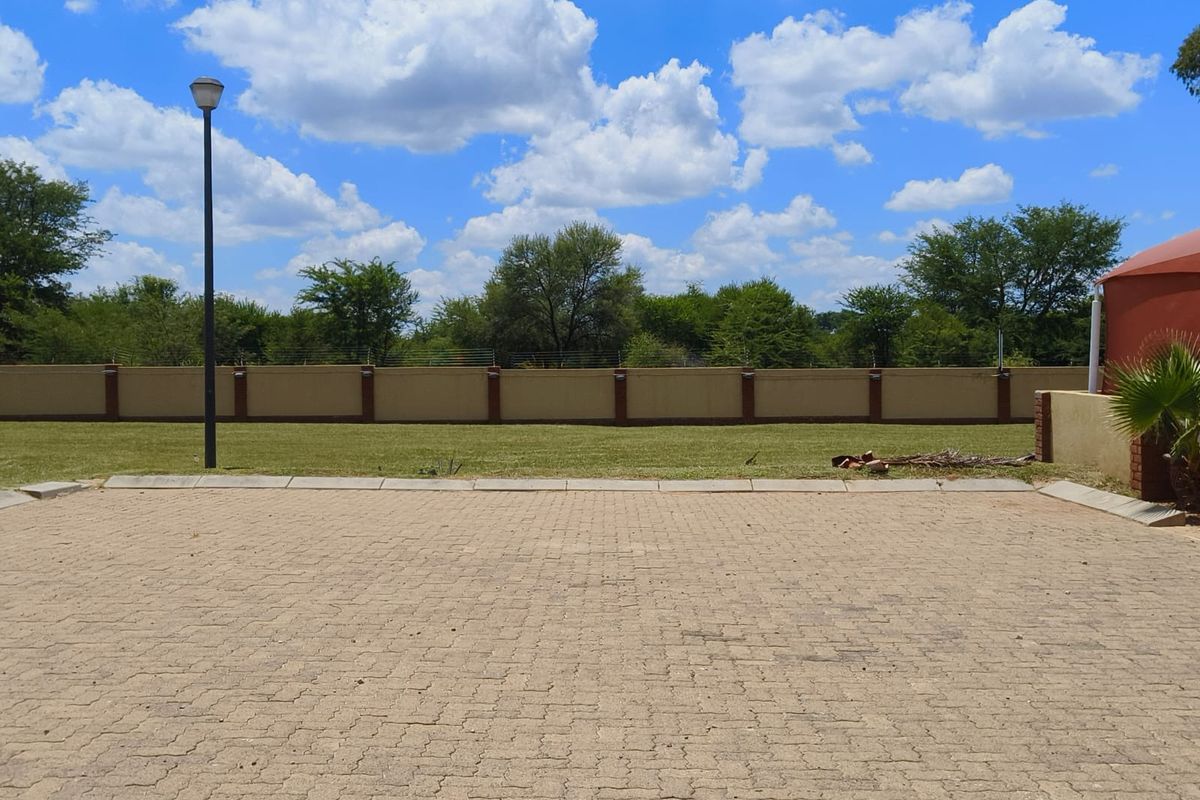 A well-maintained paved driveway area featuring a perimeter wall with electric fencing and a street lamp, set against a clear sky.