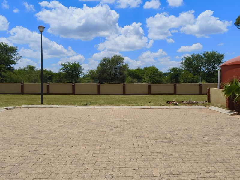 A well-maintained paved driveway area featuring a perimeter wall with electric fencing and a street lamp, set against a clear sky.