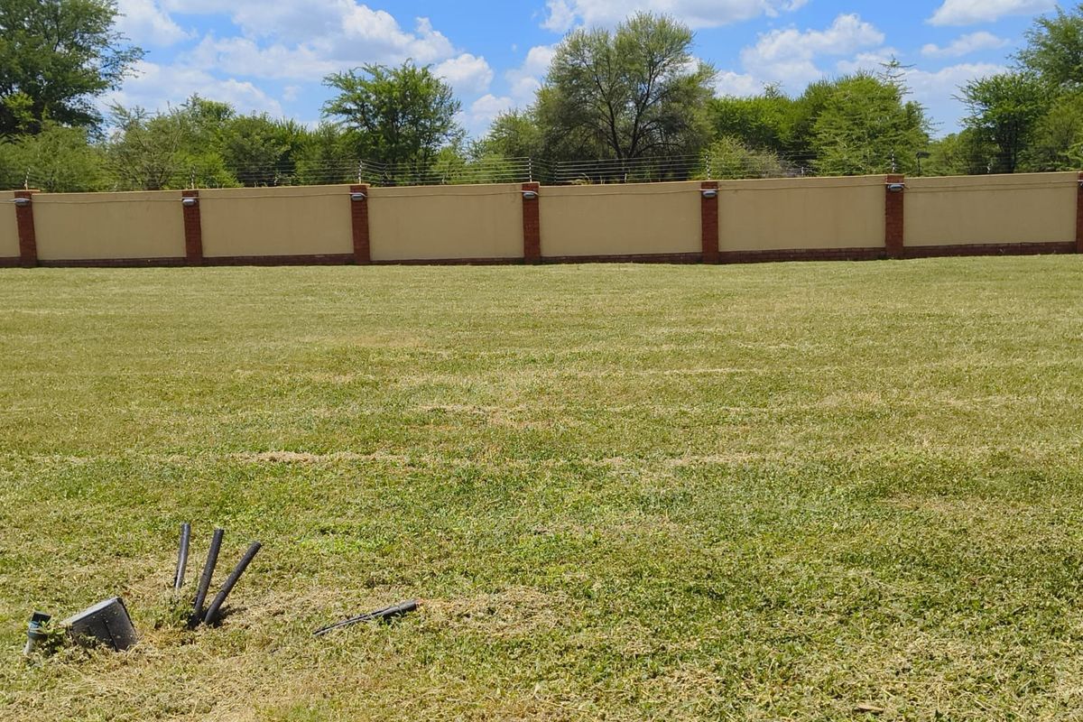 A well-maintained vacant residential plot featuring a manicured lawn, secure perimeter wall with electric fencing, and integrated wall lighting.