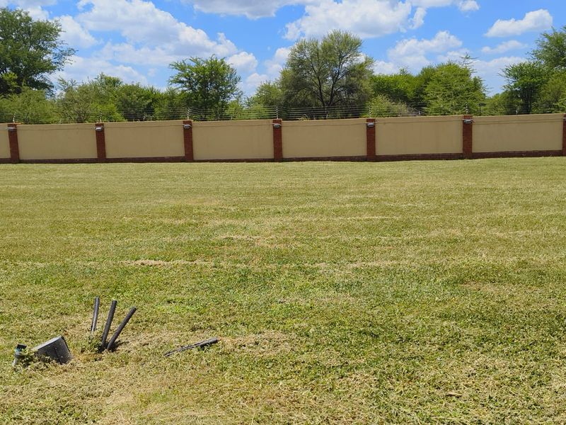 A well-maintained vacant residential plot featuring a manicured lawn, secure perimeter wall with electric fencing, and integrated wall lighting.