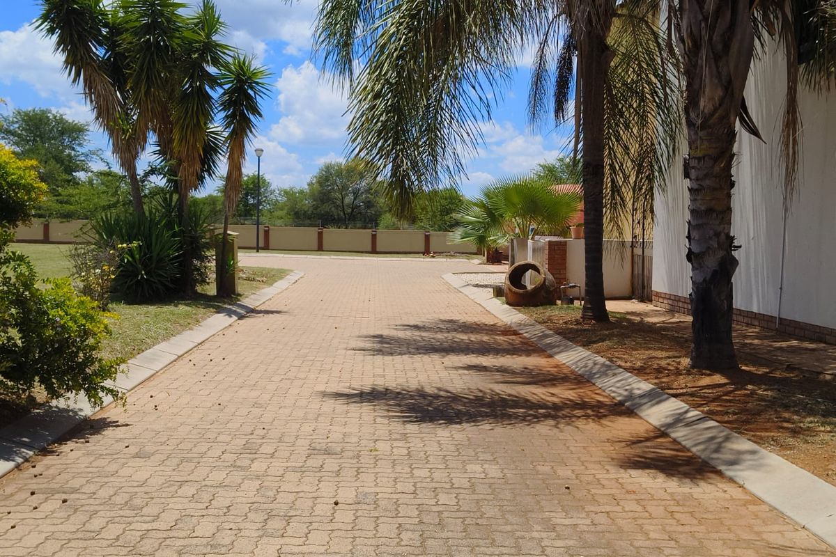 A well-maintained paved driveway leading towards the property, featuring established landscaping and a secure perimeter wall.