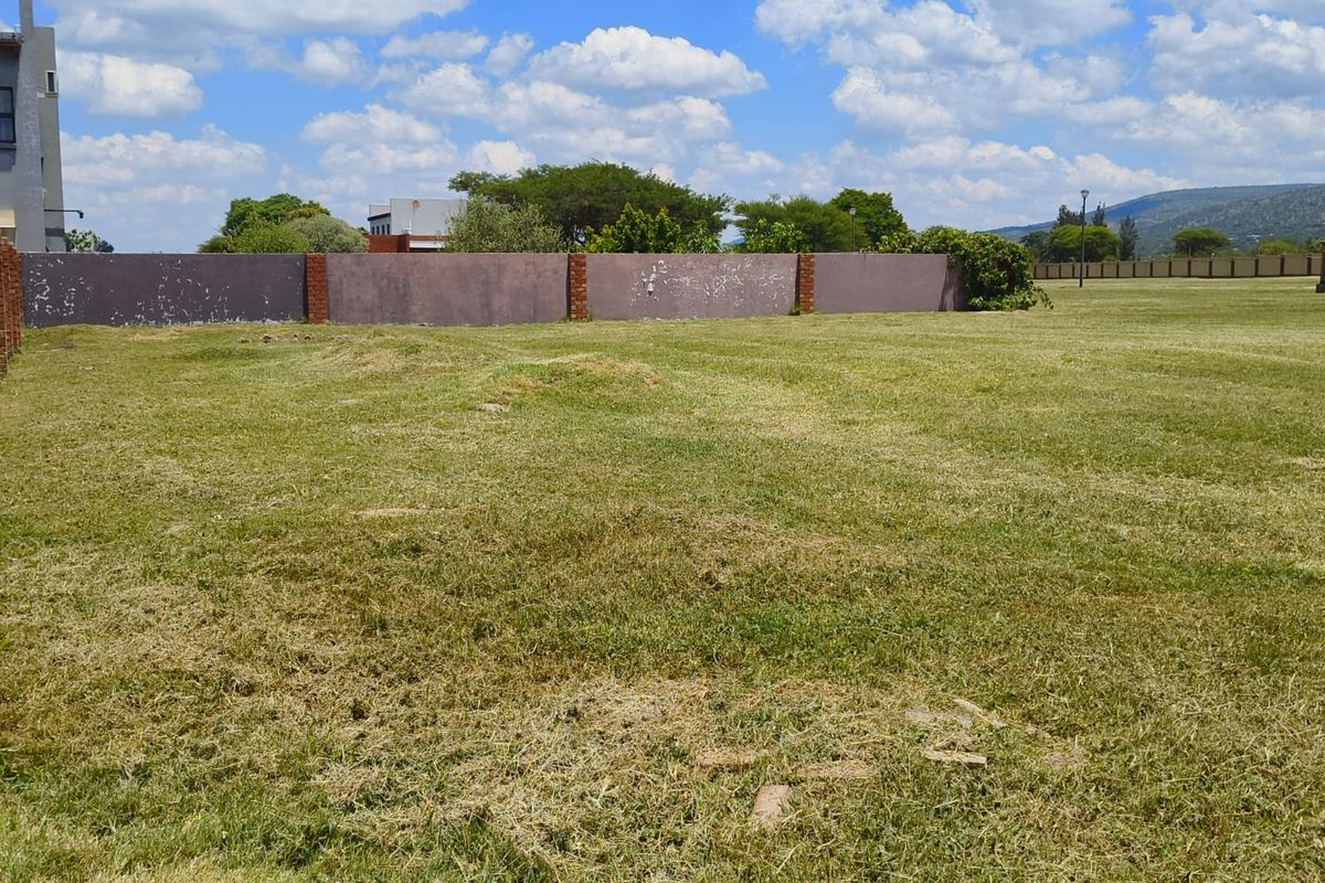 A view of a vacant residential plot featuring a grassed area and a perimeter boundary wall with brick pillars.