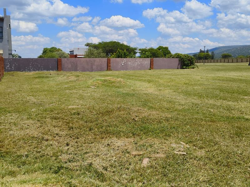 A view of a vacant residential plot featuring a grassed area and a perimeter boundary wall with brick pillars.