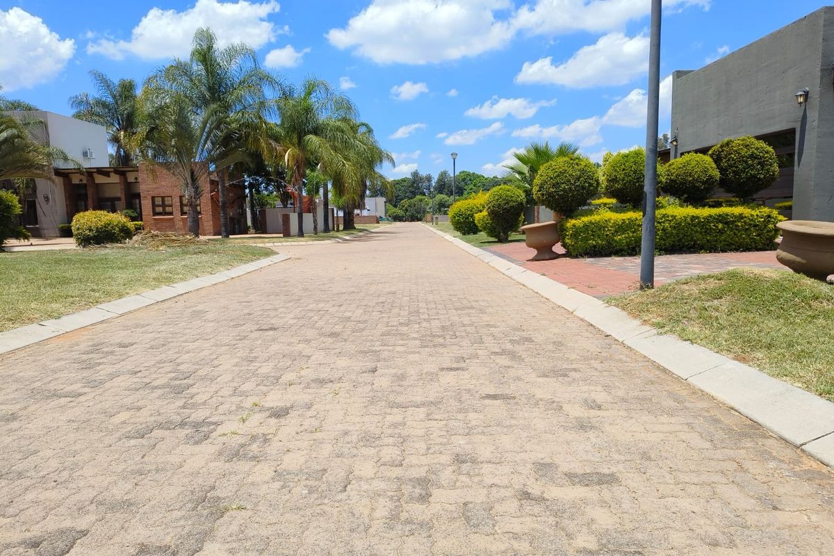 A well-maintained paved residential street view featuring manicured landscaping, concrete curbing, and established trees within a residential estate setting.