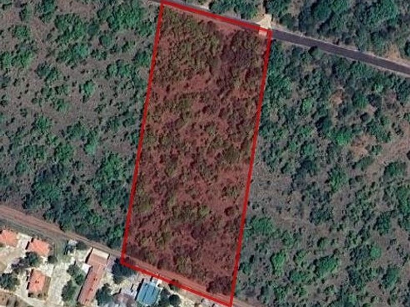 An aerial view of a vacant residential plot of land, clearly demarcated with red boundary lines, situated in a natural, undeveloped setting.