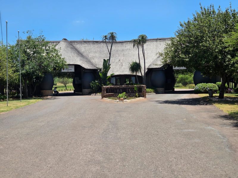 The main entrance gate to the Intaba Indle estate, featuring a distinctive thatched roof structure, paved driveway, and established landscaping.