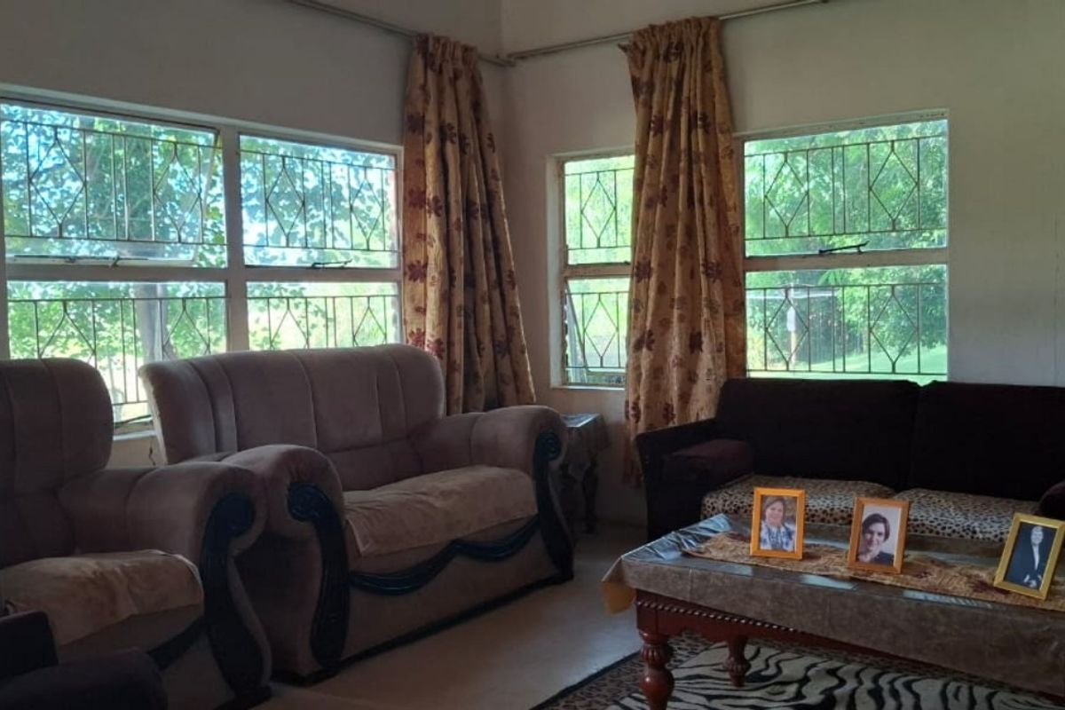 A comfortable living room featuring large windows with security bars, providing natural light and a view of the surrounding farm landscape.