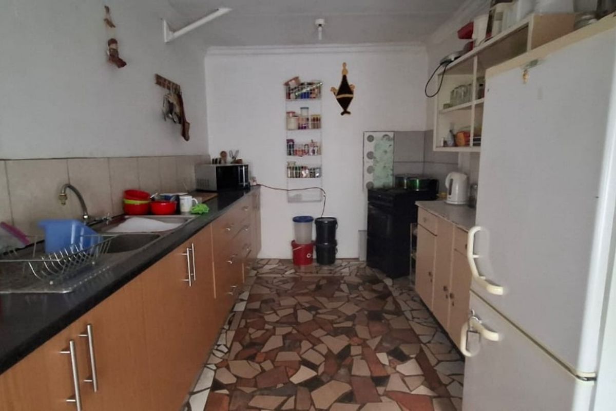 A functional galley-style kitchen featuring laminate cabinetry, stone tile flooring, and a freestanding stove, offering potential for a modern cosmetic update.