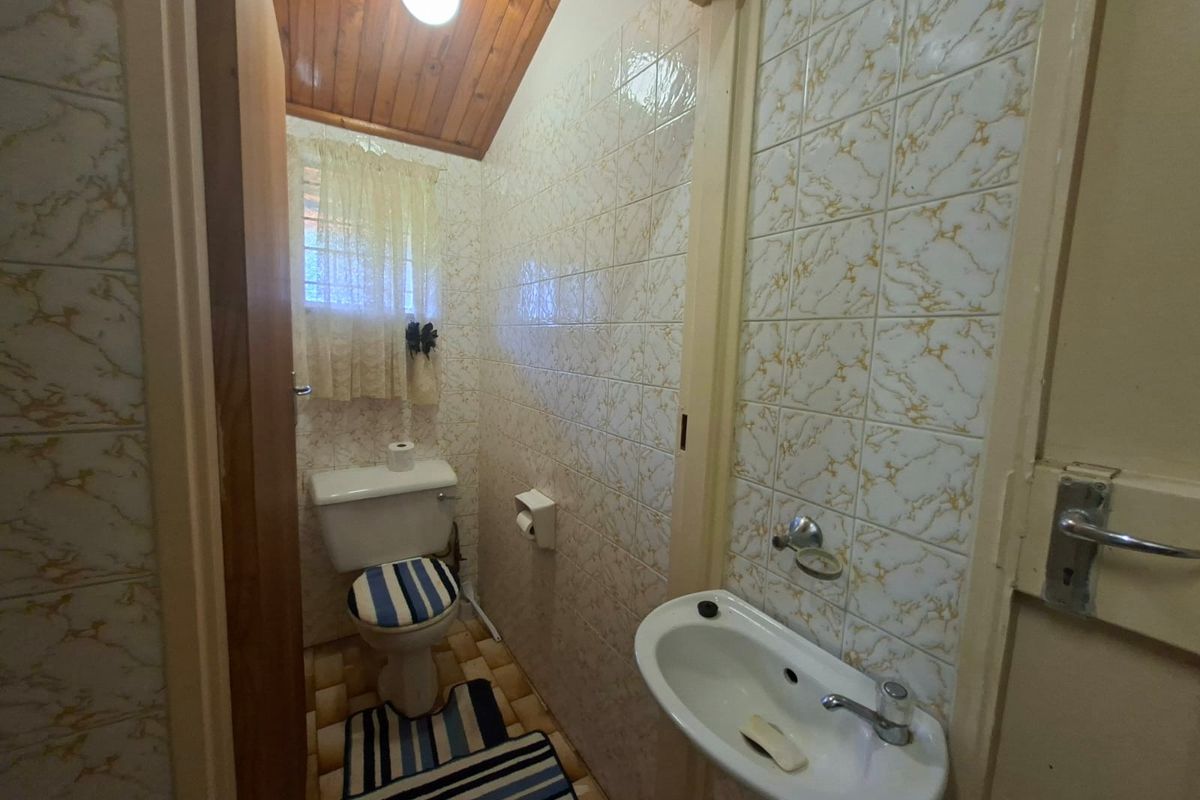 A compact guest bathroom featuring a wall-mounted basin, toilet, and timber-clad ceiling with dated wall and floor tiling.