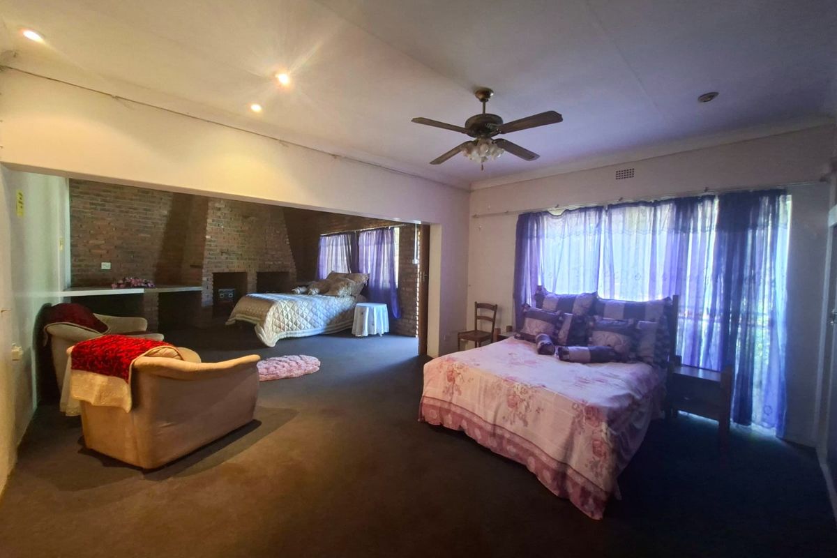 Spacious bedroom featuring an exposed brick wall, built-in fireplace, ceiling fan, and large windows with natural light.