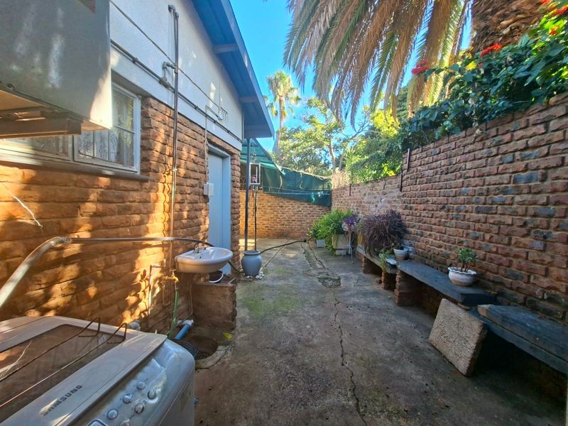 A rear exterior courtyard featuring exposed brick walls, concrete paving, and a wall-mounted utility basin, offering potential for a private outdoor space.