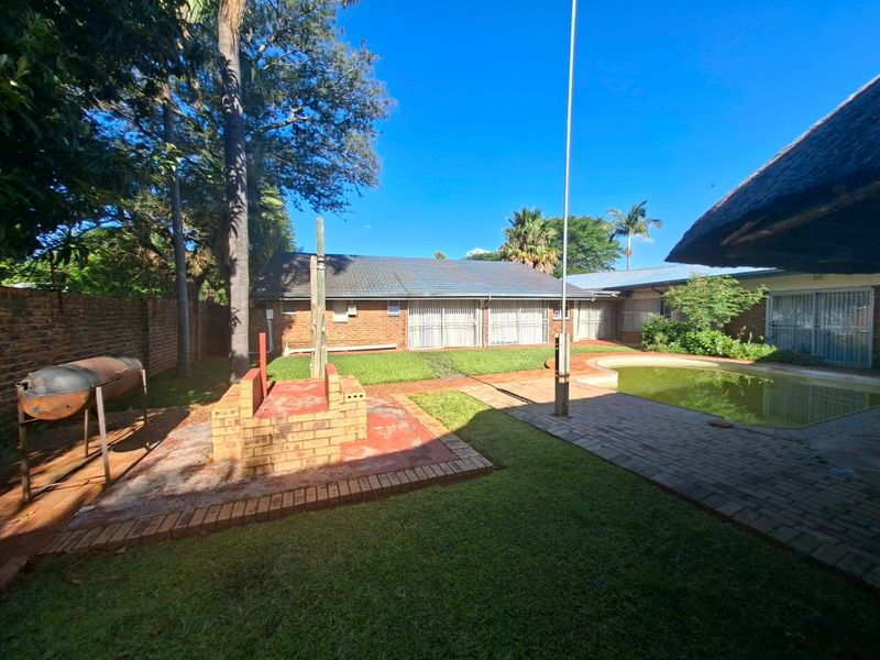 Rear garden area featuring a swimming pool, brick braai, paved patio space, and perimeter walling.