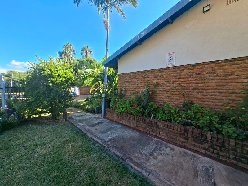 A view of the rear exterior featuring a brick facade, a built-in brick planter box, and a concrete pathway leading through the garden area.