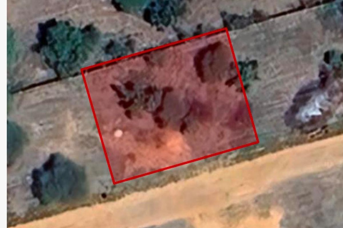 An aerial view of a vacant residential plot with a red boundary overlay indicating the property lines.