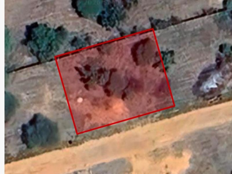 An aerial view of a vacant residential plot with a red boundary overlay indicating the property lines.