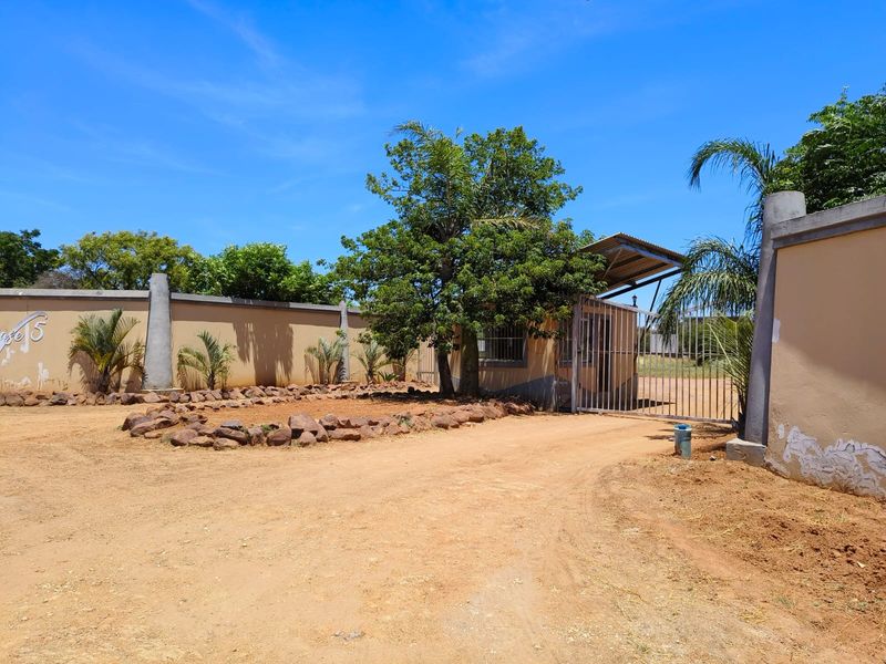 Front entrance view of the property featuring a perimeter wall, security gate, and a small guard house structure.