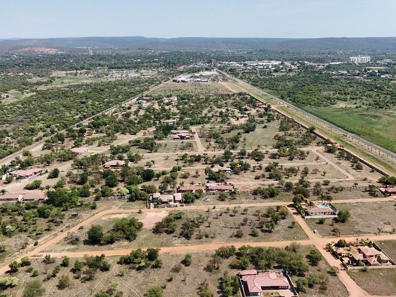 An aerial view of a residential estate featuring multiple plots, dirt roads, and surrounding natural landscape.