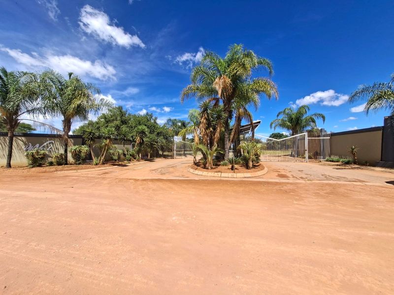 Front entrance view of the residential property featuring a gated access point, perimeter walling, and established palm tree landscaping.