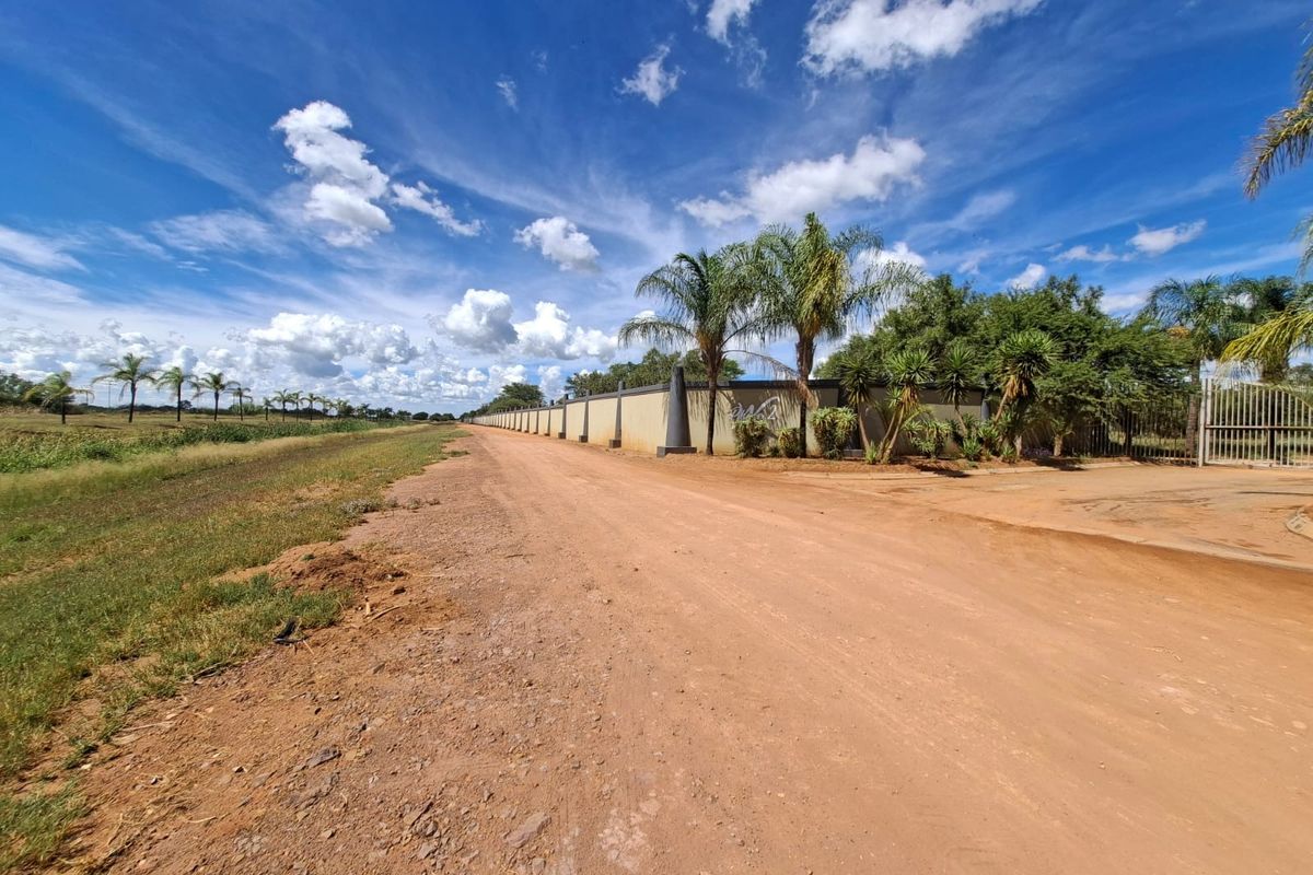 A view of the dirt road approach to the property, featuring a long perimeter wall and gated entrance.