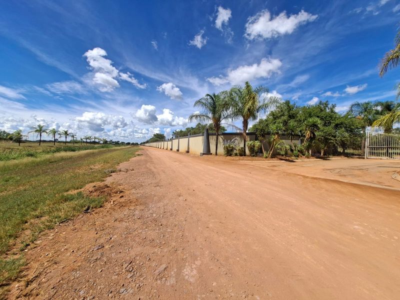 A view of the dirt road approach to the property, featuring a long perimeter wall and gated entrance.